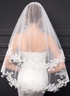 the back of a bride's veil with white flowers and leaves on it, against a black background