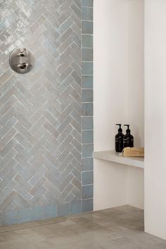 a bathroom with white walls and grey tiles on the shower wall, along with two black soap dispensers