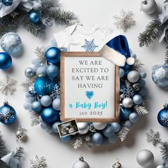 a baby boy announcement surrounded by blue and silver christmas ornaments with a sign that says we are excited to say we are having a baby boy