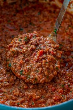 a ladle full of meatballs and sauce in a blue bowl with a spoon