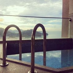 an empty swimming pool next to a large window with the ocean and mountains in the background