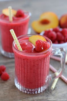 two glasses filled with raspberry smoothie on top of a wooden table next to fruit