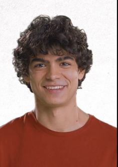 a young man with curly hair smiles at the camera while wearing an orange t - shirt