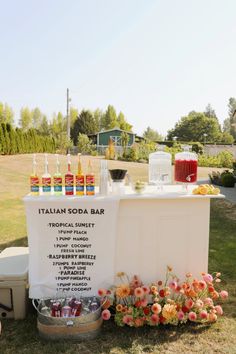 an outdoor bar set up in the grass with flowers and bottles on it's side