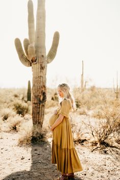 a woman standing in front of a cactus with her back to the camera, wearing a yellow dress