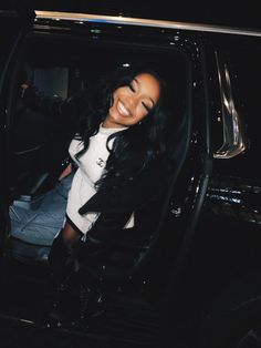 a woman sitting in the passenger seat of a black car with her arm out and smiling