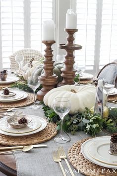 a dining room table set for thanksgiving with white pumpkins, greenery and candlesticks