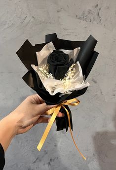 a hand holding a black and white flower bouquet with yellow ribbon tied around the top