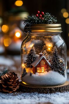 a glass jar filled with snow and christmas lights on top of a wooden table next to a pine cone