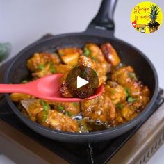 a pan filled with meat and vegetables on top of a stove burner next to a red spatula