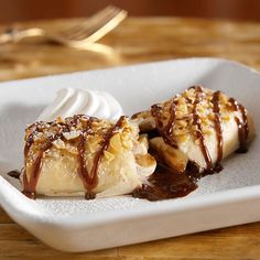 two bananas covered in chocolate sauce and whipped cream on a white plate next to a fork