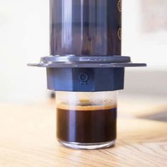 a coffee cup sitting on top of a wooden table next to a metal container with liquid in it