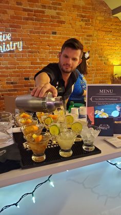 a man pouring drinks into glasses at a bar with brick wall in the back ground