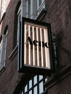 an acne sign hanging off the side of a building in front of a window