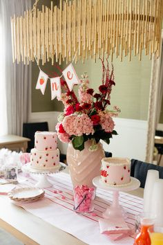 a table topped with pink and red cakes next to a tall vase filled with flowers