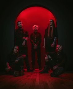 a group of men standing next to each other in front of a red wall with blood on it