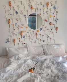 a bed with white sheets and flowers on the wall above it is shown in front of a round mirror