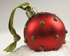 a red ornament sitting on top of snow with a green ribbon around it