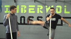 two men standing in front of a gym wall holding poles and talking to each other