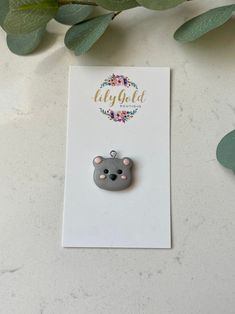 a brooch with a bear on it is sitting next to some leaves and flowers