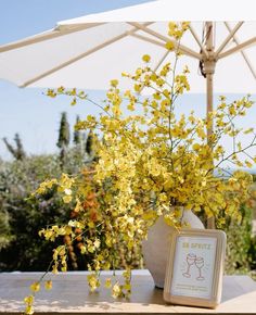 a vase with yellow flowers sitting on top of a table next to an open umbrella