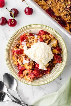 a bowl filled with ice cream and cherries next to a pan of baked goods