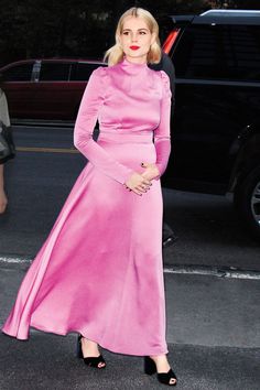 a woman in a long pink dress is standing near a car and wearing black heels