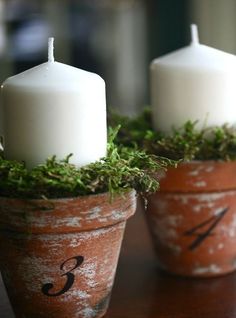 two white candles sitting in small clay pots with moss growing on the sides and numbers painted on them