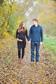 a man and woman holding hands walking through the leaves in an autumn forest with text overlay that reads, maternity session in a fogy field