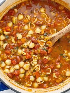 a pot filled with pasta and sauce on top of a blue table cloth next to a wooden spoon