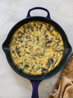 an omelet with mushrooms and cheese in a blue cast iron skillet on a marble surface