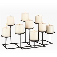 twelve white candles are lined up in a row on a black metal stand with one candle lit