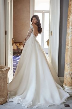 a woman in a wedding dress is standing near an open door with her back to the camera