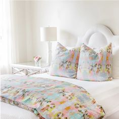 a white bed topped with lots of pillows next to a night stand and window sill