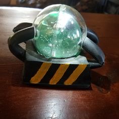 a green glass ball sitting on top of a black and yellow stand next to a wooden table