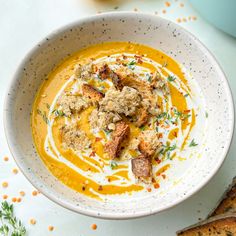 a white bowl filled with carrot soup next to some slices of bread on a table