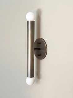 a wall mounted light on the side of a white wall with two balls attached to it