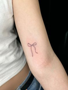 a woman's arm with a small bow tattoo on the left side of her arm