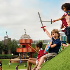 two children playing with toy planes on the grass in front of an amusement park area