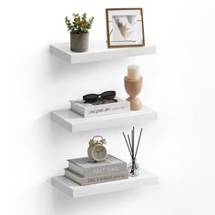 three white floating shelves with books, vases and other items on each shelf in the corner