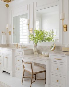 a white bathroom with gold accents and marble counter tops, along with a chair that has a plant in it