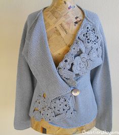 a blue jacket with crocheted flowers on the front and back, sitting on top of a mannequin