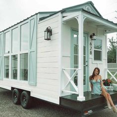 a woman is sitting on the back of a tiny white house with windows and doors