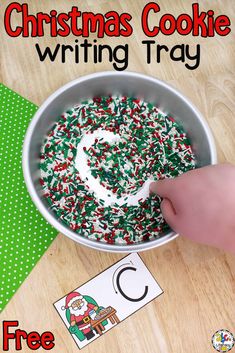 a christmas cookie writing tray is shown with the letter c on it and a hand reaching for sprinkles