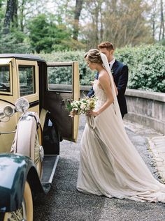 a bride and groom standing next to an old car