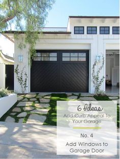 a white house with black garage doors and grass on the front lawn in front of it