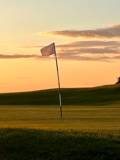 an empty golf course at sunset with a flag in the foreground and green grass on the far side