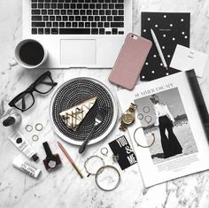 the contents of a woman's purse laid out next to her laptop on a marble table