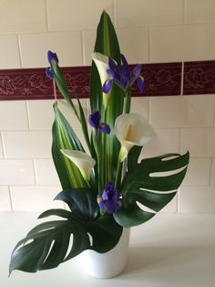 a white vase filled with purple and white flowers on top of a table next to a tiled wall