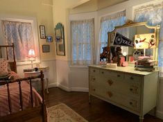 a bedroom with a bed, dresser and mirror on the wall next to two windows